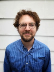 Headshot of Ben wearing glasses and a blue button up shirt.