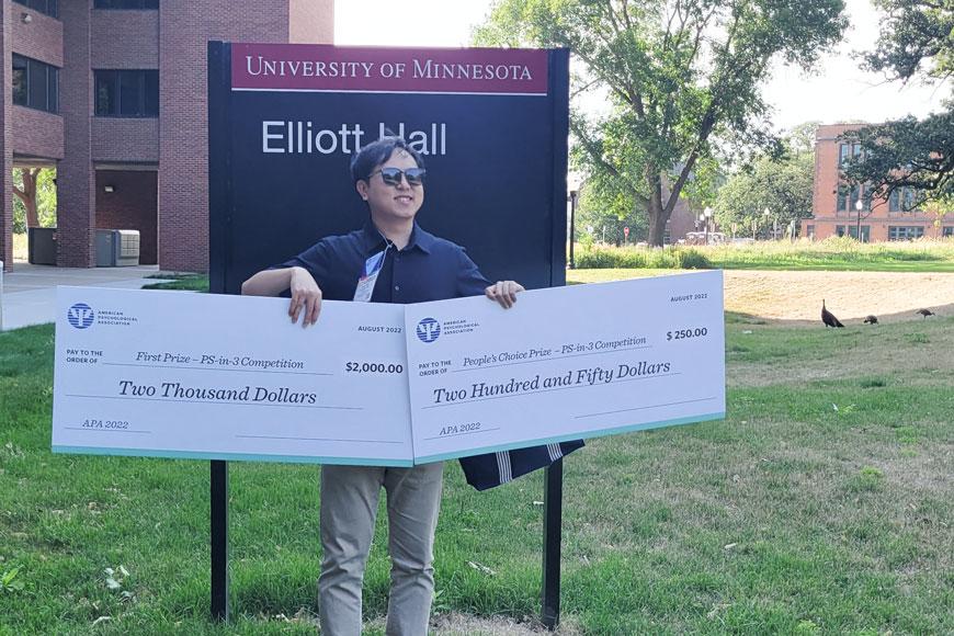 Walter Wu with award winning checks in front of Elliott Hall