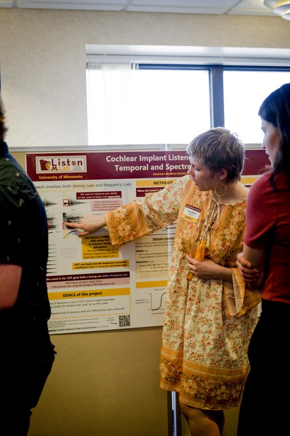 Woman point at her research poster while explaining research to attendees