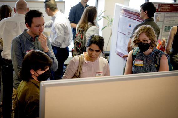 Three people listening to a student describe her research poster.