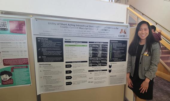 Angela Cao wearing a black dress and gray blazer, standing to the right of her research poster.