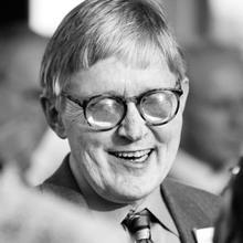 Man smiling wearing glasses, a suit and tie.